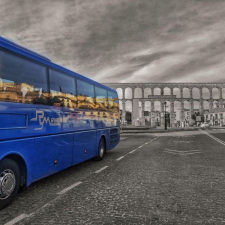 Autobús grande azul con acueducto gde Segovia al  fondo